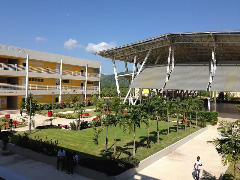 Un campus universitaire en Haïti, bâtiments de classes, grande structure couverte et palmiers, avec les montagnes en arrière-plan